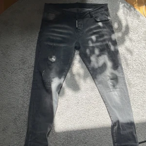 Svarta Dsquared2 jeans  - Säljer ett par svarta jeans från Dsquared2 i storlek 52. Jeansen har coola slitningar och en tvättad look, med Dsquared2-logga vid gylfen. Modellen är smalare i benen och materialet är klassisk denim.