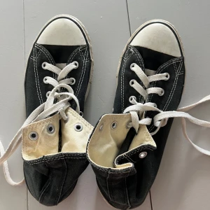 Svarta Converse Chuck Taylor All Star - Klassiska svarta Converse Chuck Taylor All Star med vit tå och vita snören. Skorna har rund tå, platt sula och tydliga vita sömmar. Märket syns på sidan. Ovandel och foder i textil, yttersula i syntet. Perfekta för en cool och avslappnad stil. Storlek 35. 