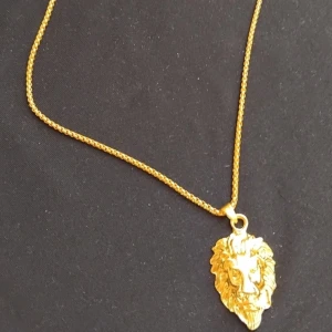 Guldhalsband med lejonhänge - Coolt halsband i guld med ett detaljerat lejonhänge. Kedjan är tunn och glänsande, perfekt för dig som vill sticka ut med ett djuriskt statement. Passar både till streetwear och mer dressade outfits.