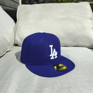 Blå LA Dodgers keps från New Era - Snygg blå LA Dodgers keps från New Era med klassisk rak skärm och broderad vit LA-logga framtill. MLB-logga baktill och New Era-logga på sidan. Kepsen är i modellen 59FIFTY och har en stilren look som passar perfekt till streetwear.                                          Kepsen är helt ny och har aldrig använts.