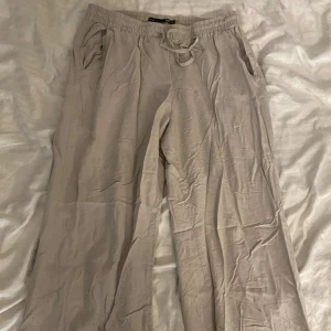 Beiga linnebyxor  - Snygga och luftiga beiga linnebyxor från 157 med resår och snörning i midjan. Byxorna har raka ben och sidofickor.