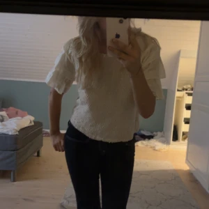 Vit blus med volangärmar - Supersöt vit blus med strukturmönstrad framsida och breda volangärmar. Toppen är lite croppad och har en luftig känsla, perfekt för dig som gillar romantiska detaljer. Materialet känns som bomull och ärmarna har en snygg volangeffekt som sticker ut.
