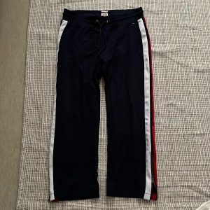 Tommy Jeans marinblå träningsbyxor L - Marinblå träningsbyxor från Tommy Jeans med vita och röda ränder längs sidorna. Byxorna har snörning i midjan, har använt få gånger.