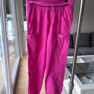 Rosa cargopants  - Säljer ett par chockrosa cargopants med elastisk midja och snörning. Byxorna har flera stora fickor på sidorna och muddar vid bensluten. 