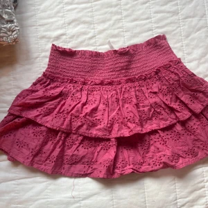 Rosa volangkjol från Stradivarius XS - Supersöt rosa kortkjol från Stradivarius i bomull med broderade blommor och volanger. Kjolen har smock i midjan för en bekväm passform och är fodrad med shorts under. Perfekt för sommarens alla äventyr!