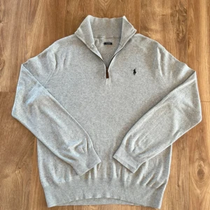 Grå half zip tröja från Polo Ralph Lauren - Snygg ljusgrå långärmad tröja från Polo Ralph Lauren med half zip och broderad logga på bröstet. Mjuk bomullskvalitet och klassisk passform, perfekt till lager-på-lager. Hög krage och ribbade muddar för extra stilpoäng.