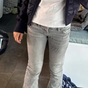 Grå lowrised bootcut jeans - Säljer ett par grå bootcut jeans med snygga vita kontrastsömmar på bakfickorna. Storlek 152-158, inget slitage och är i väldigt bra skick!