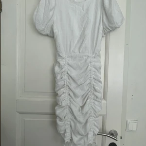 Vit omlottklänning från NLY Trend - Supersnygg vit kortklänning från NLY Trend med puffärmar och dragsko längs hela framsidan som ger en cool rynkad effekt. Klänningen har rund halsringning, dragkedja bak och är tillverkad i ett lätt bomullsliknande material. Perfekt för dig som vill sticka ut!