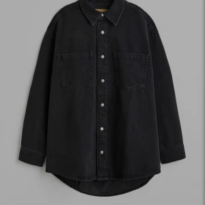 Oversized svart denimskjorta - Snygg oversized svart denimskjorta med klassisk krage, två stora bröstfickor och knappar framtill. Skjortan har långa ärmar och är tillverkad i jeansmaterial. Perfekt för en avslappnad och trendig look. Den är från HM och orginalpris är 300 kr. Den har använts bara 1 eller 2 gånger men annars är den helt ny. 