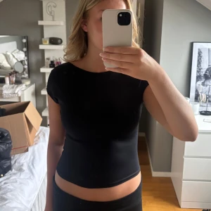 Svart  topp med öppen rygg - Säljer en svart topp med korta ärmar och en djup, öppen rygg. Nästintill oanvänd från Bikbok. Toppen har en enkel och stilren design i stretchigt material som sitter tight mot kroppen. Perfekt för dig som vill ha en basic men ändå snygg topp med det lilla extra. 