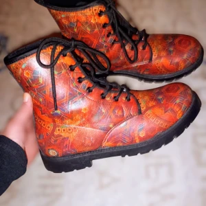 Mandala Boots  - Unika Mandala kängor i rött och orange med geometriskt mönster och svarta detaljer. Skorna har svart snörning, grov platt sula och rund tå. Perfekta för dig som vill sticka ut med din stil och gillar färg och mönster. Konstgjort läder (100 % veganskt)  Storlek 41. Nypris 1499 kr. Säljes för 600 kr. 