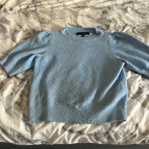 Ljusblå stickad tröja Vero Moda - Supersöt ljusblå stickad tröja från Vero Moda med korta puffärmar och ribbade kanter. Perfekt för dig som gillar en feminin och trendig look. Mjuk och skön, passar till både jeans och kjol.