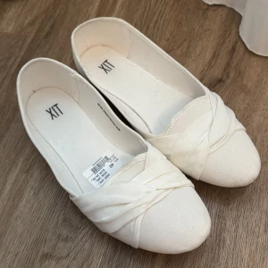 Vita ballerinaskor  - Snygga vita ballerinaskor från XIT i storlek 40. Skorna har en rund tå och ett elegant omlottband framtill. Tillverkade i textil med en platt sula i gummi. Perfekta för en clean och stilren look. Skorna är använda vid endast ett tillfälle! Hör av er vid frågor💓