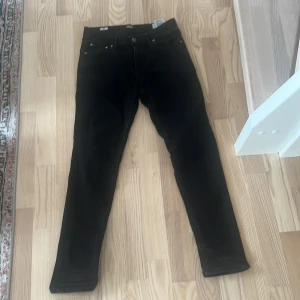Svarta Jack and Jones jeans  - Svarta slim jeans från Jack & Jones, modell Liam. Klassisk femficksdesign med snygga detaljer på fickorna och svart patch bak i midjan. Jeansen är i stretchigt material för en slim och bekväm passform.