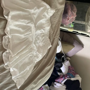 Vit volangkjol från SHEIN - Supersöt vit kortkjol från SHEIN med volangkant och elastisk midja. Kjolen är i ett lätt och flowy material som känns perfekt för varma dagar. Enkel att matcha med crop tops eller hoodies för en chill vibe.har en underkjol inuti.