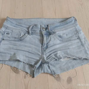 Ljusblå lågmidjade jeansshorts från G-Star RAW - Snygga ljusblå jeansshorts från G-Star RAW med råa, fransiga kanter och slitna detaljer. Klassisk femficksmodell med bälteshällor och knappgylf. Perfekta för sommardagar när du vill ha en avslappnad och cool look. De är avklippta jeans i storlek 27/32 men passar xs-s❤️skriv för funderingar💗