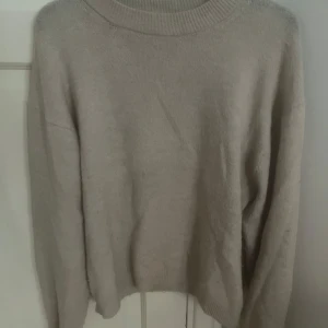 Beige stickad tröja från H&M - Enkel och stilren beige stickad tröja från H&M i storlek S. Tröjan har rund halsringning, långa ärmar och ribbade muddar vid hals, ärmslut och nederkant. Perfekt för lager-på-lager och chill vibes.