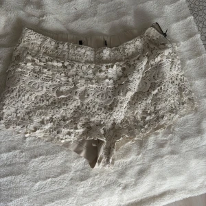 Beige spets-shorts med blommigt mönster - Superfina beige shorts med blommig spets och snyggt fodrad insida. De har en hög midja och dragkedja i sidan för en clean look. Perfekta för sommarens varma dagar när du vill sticka ut med en romantisk vibe.