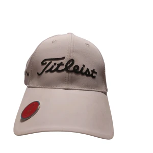 Vit Titleist keps Pro V1 - Snygg vit keps från Titleist med svart logga framtill och texten PRO V1 på sidan. Kepsen har även FJ-logga på andra sidan och en röd markör på skärmen. Perfekt för golfbanan och sportig stil. Justerbar baktill för bästa passform.