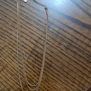 Tunt halsband i guld och koppar - Snyggt halsband med tre tunna kedjor i guld och kopparfärg. Kedjorna har olika textur och ger en cool lager-på-lager look. Perfekt för att addera lite extra stil till din outfit.