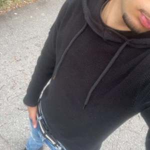 Svart stickad hoodie med huva - Säljer en svart stickad hoodie med huva och snörning. Tröjan har långärmade och är perfekt för dig som gillar en enkel och stilren look. Passar till jeans och sneakers för en chill vibe. Och så har den en litet håll i armhålan 