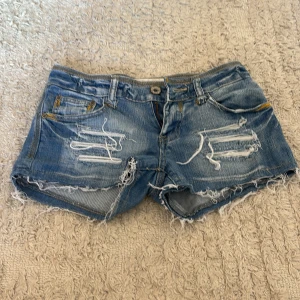 Blå jeansshorts med slitningar - Säljer ett par blå jeansshorts med, fransiga kanter och tydliga slitningar både fram och bak. As snygga shorts nu till sommaren