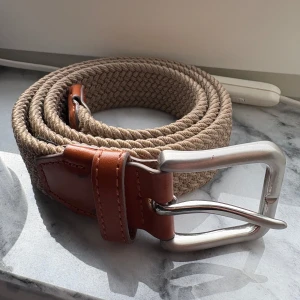 Grisch bälte - Säljer ett beige flätat bälte från Jack & Jones med detaljer i brunt skinn och ett robust silverfärgat spänne. Perfekt accessoar för att lyfta din outfit med en stilren touch.