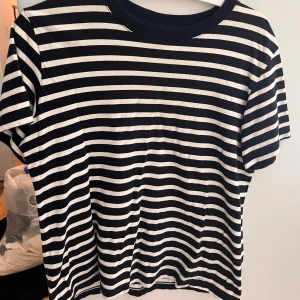 Randig t-shirt från H&M, svart/vit - Snygg svart och vit randig t-shirt från H&M i storlek S. Klassisk modell med rund hals och korta ärmar. Perfekt till jeans eller shorts för en chill och stilren look. Gjord i mjuk bomull som känns skön mot huden.