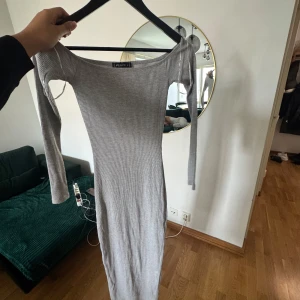 Ljusgrå ribbad långklänning FB Sister - Säljer en ljusgrå, ribbad långklänning från FB Sister i storlek S. Klänningen har lång ärm och en tight passform med offshoulder-skärning. Perfekt för dig som gillar minimalistisk och stilren look.