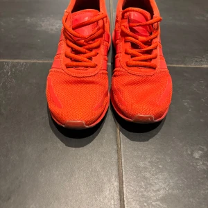 Röda Adidas Los Angeles sneakers - Snygga röda Adidas Los Angeles sneakers med klassiska tre ränder på sidan. Skorna har ovandel i mesh och syntet, snörning och platt sula. Perfekta för dig som vill sticka ut med en färgstark look.