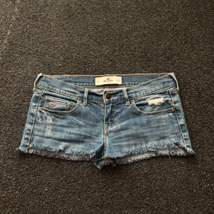 Hollister jeansshorts  - Snygga blå Lågmidjade jeansshorts från Hollister!! Snygga slitna detaljer både fram och bak. W26, skriv om ni har några funderingar<3