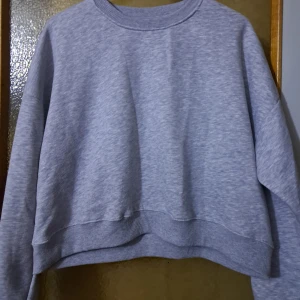 Grå croppad sweatshirt - En basic grå croppad sweatshirt med rund hals och långa ärmar. Tröjan har en loose fit och är tillverkad i mjuk bomullsblandning. Perfekt för en chill och avslappnad stil. Varm och skön :)