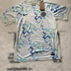 Inter Milan Nike fotbollströja  - Inter Milan fotbollströja från Nike i vitt med ljusblått och blått geometriskt mönster. Tröjan har korta ärmar, broderat klubbmärke och Nike-logga på bröstet. Tillverkad i lätt och ventilerande material, perfekt för match eller träning.
