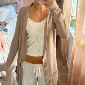 Beige kofta med fickor - Säljer en beige, långärmad kofta med öppen front och två praktiska fickor. Koftan har en loose passform och är tillverkad i mjukt bomullsmaterial, perfekt att slänga över en topp för en chill och avslappnad look.