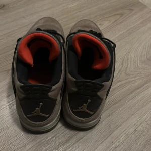 Nike Air Jordan 4 Taupe Haze - Nike Air Jordan 4 Taupe Haze med gråbrun mocka, svarta detaljer och meshpaneler. Insidan har en snygg kontrast i rödorange. Klassisk Jumpman-logga på plös och häl. Perfekta sneakers för dig som vill sticka ut med stilren design och coola materialval.