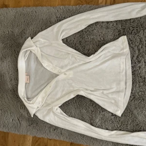 Vit ribbad tröja med knappar från Nelly - Säljer en vit ribbad tröja med knappar från Nelly i storlek S. Tröjan har lång ärm, v-ringning och knappar framtill. Säljer då den knappt används.