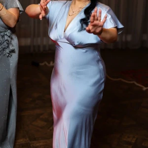 Ljusblå långklänning med v-ringning - Säljer en elegant ljusblå långklänning med v-ringad hals och korta ärmar. Klänningen har en mjuk, glansig yta som ger en lyxig känsla och följer kroppen snyggt. Perfekt för dig som vill sticka ut med en stilren look och skön passform.