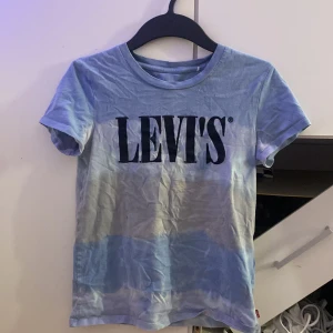 Blå Levi's t-shirt med logga - Snygg blå t-shirt från Levi's med stor svart logga framtill. T-shirten har korta ärmar, rund halsringning och är gjord i mjuk bomull. Perfekt för en chill och avslappnad stil. Även målat den hemma men det håller vid tvättning. 