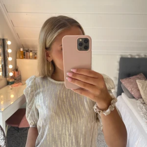 Glittrig blus från Holly & Whyte - Säljer en jättefin glittrig blus från Holly & Whyte med guldiga detaljer. Blusen har puffiga korta ärmar och rund halsringning. Materialet är lätt och skimrande, Perfekt för utekvällar eller att man bara vill känna sig extra fin! Storlek S men skulle säga att den kan sitta som en S/M då den är ganska stor.🥰🥰 endast använd 2 gånger därav bra skick!