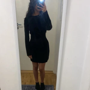 Svart sammetsklänning med cut out - Snygg svart kort sammetsklänning med lång ärm och en cool cut out-detalj i midjan, dekorerad med glittriga pärlor. Tight passform som framhäver figuren och ger en trendig look. Köpt i Zara utomlands, endast använd 1 gång. 
