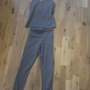 Mörkgrå träningsset från soc - Supersnyggt mörkgrått träningssett från soc med korsade band i ryggen på toppen. Toppen är ärmlös och settet har en slim passform som sitter skönt under träningspasset. Materialet är mjukt och stretchigt, perfekt för gym eller yoga. Toppen är i storlek S och leggings är storlek xs.