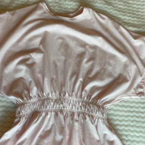 Topp med tajt runt midjan - Supersöt ljusrosa topp från 157 i mjuk bomull. Toppdn har rund hals, korta ärmar och en snygg smockad midja. Perfekt för varma dagar. Använd 1 gång 