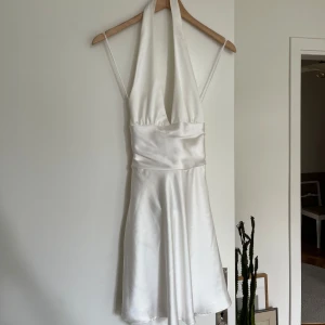 Vit satin klänning med rosett XS - Supersnygg vit kortklänning från Zara i glansigt satinmaterial. Klänningen har halterneck, djup v-ringning och öppen rygg med en stor rosett bak. Denna har slutats säljas på Zara 💕 helt ny aldrig använd och prislappen är kvar!