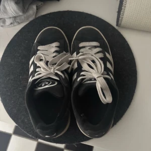 Adidas Campus svarta 00s - Skorna är välanvända men ser fortfarande jättebra ut. Det finns ett hål inuti båda skorna🤍🤍