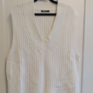 Vit stickad väst från Gina Tricot - Vit stickad väst med bred v-ringning från Gina Tricot. Västen har en chunky ribbstickad struktur och är ärmlös med en avslappnad passform. Perfekt att styla över en skjorta eller t-shirt för en trendig lager-på-lager-look.