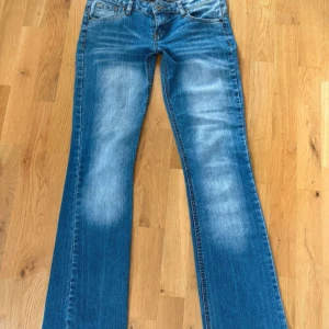 Blå bootcut jeans från Mudd - Snygga blå bootcut jeans från Mudd med slitningar och ljusa partier framtill. Klassisk femficksmodell med låg midja och coola detaljer på bakfickorna. Midje mått:ca38cm Gren:ca14cm Ben:ca97cm  Innerbens längd:ca 21cm