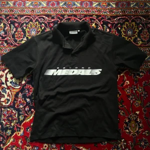 Svart Beyond Medals t-shirt med tryck - Svart t-shirt från Beyond Medals med klassisk krage och stort vitt tryck på bröstet. T-shirten har korta ärmar och en rak passform. Materialet känns som bomull och ger en skön känsla. Perfekt för dig som gillar streetwear och tydliga loggor.