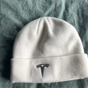 Vit stickad mössa från Tesla - Snygg vit mössa från Tesla med uppvikt kant och stilren logga framtill som jag säljer då jag inte har använt den och inte kommer göra det.  Mössan går inte att få tag på förutom om man då väljer att köpa en Tesla bil men annars så går det ej att köpa hos Tesla.