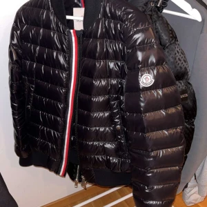 Svart Moncler pufferjacka - Säljer nu denna snygga svarta pufferjacka från Moncler för att den tyvärr inte kommer till användning. Jackan är självklart äkta och taggen fungerar. Den har en  glansig finish med quiltad design och den klassiska moncler loggan på ärmen samt ribbade muddar. Perfekt för dig som vill ha en stilren och varm jacka, funkar på som höstjacka!  Storlek 2 passar S/M  Jackan är Ny skick då den endast är använd några gånger.  Nypris är 12 000kr. 