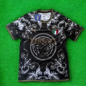 Italien Versace x Puma svart fotbollströja - Unik svart fotbollströja från Puma och Versace med Italiens landslagsemblem. Tröjan har korta ärmar, guldiga detaljer och ett iögonfallande barockmönster i vitt och grått. Tillverkad i lätt och glansigt material, perfekt för dig som vill sticka ut på planen.